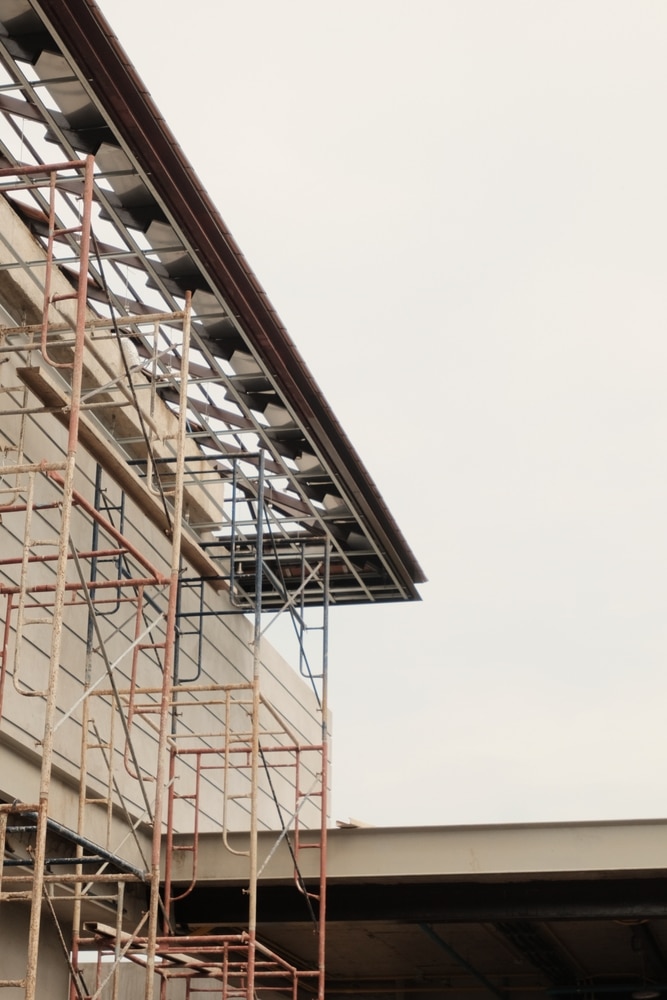 Échafaudage et construction de toiture sous ciel gris Échafaudage métallique rouillé devant la façade d'un bâtiment en construction. Vue détaillée de la charpente de toiture inachevée.