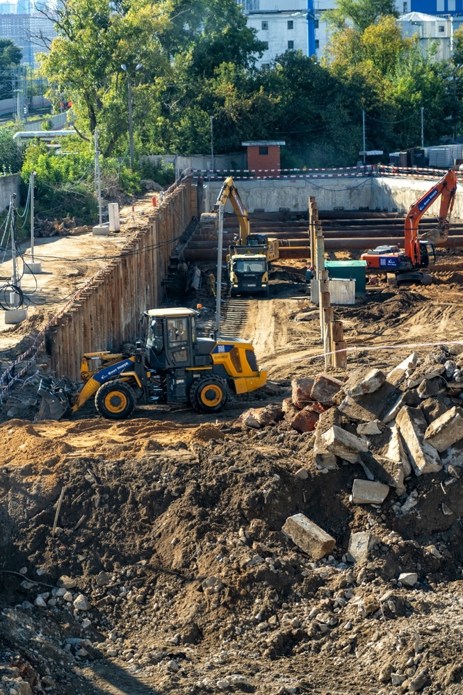 Chantier d'excavation profonde : Machines lourdes et palplanches. Chantier d'excavation profonde avec palplanches métalliques. Une chargeuse K. Beun & Meyer déplace la terre devant deux pelles et des tuyaux.