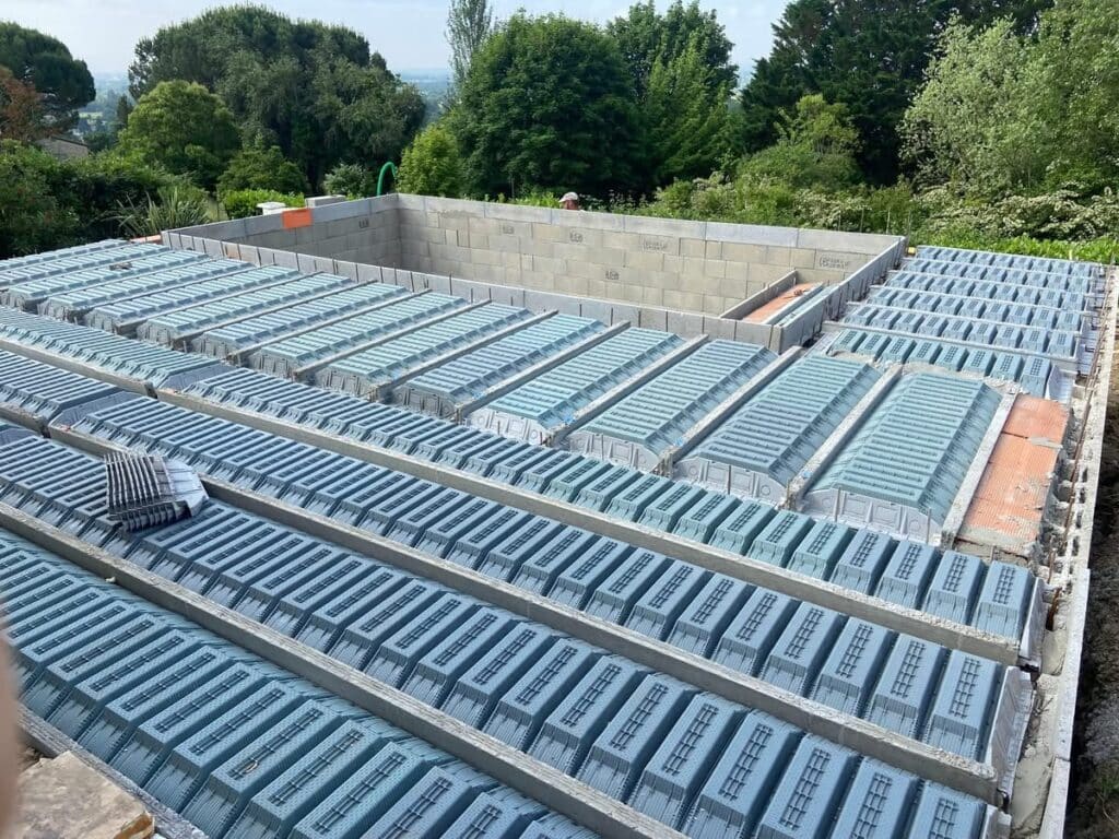 Plancher hourdis : construction de dalle avec entrevous isolants. Chantier : plancher en construction avec rangées de coffrages (entrevous) isolants bleus sur poutrelles béton. Murs en parpaings.