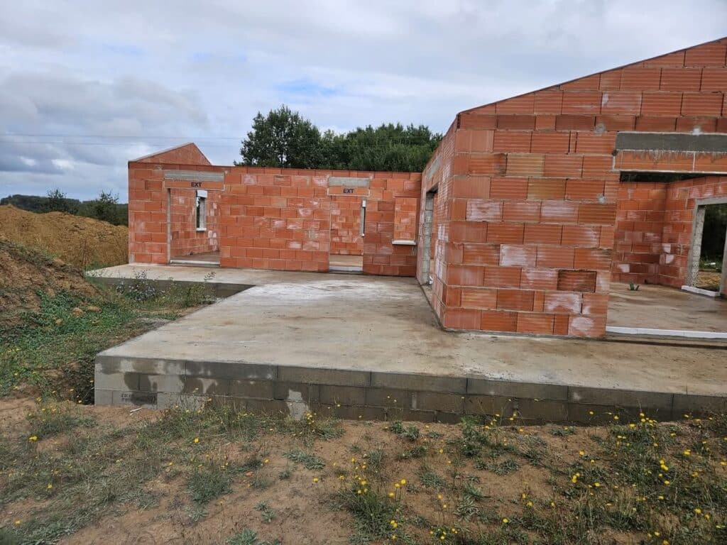 Construction maison : le gros œuvre en briques rouges Gros œuvre d'une maison neuve, murs en briques rouges sur fondation en parpaings. Dalle de béton et ouvertures (EXT) visibles.